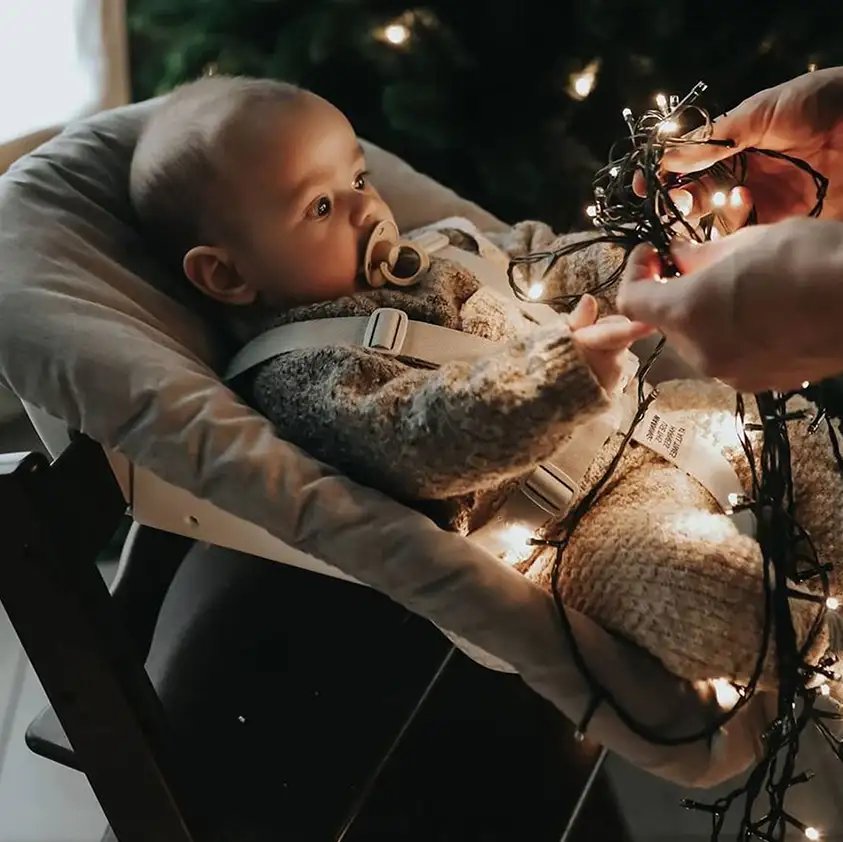 Tripp Trapp z leżaczkiem niemowlęcym, maluch trzymający świąteczne lampki w dłoniach